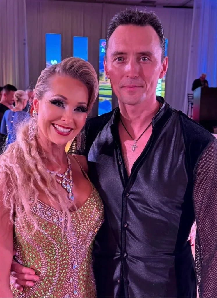 Kara Lee in a green and gold rhinestone Latin dress with her teacher Dmitry Ilyushenov at a competition