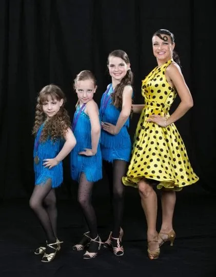 Three young students in matching blue fringe costumes with their coach